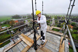 Het stalen ornament waarop de windhaan staat, is danig verweerd. Roest moet worden afgekrabd, waarna een coating wordt aangebracht